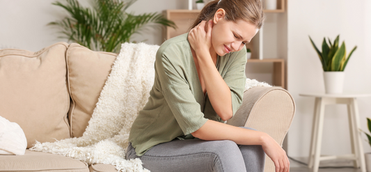 Woman sitting on couch holding her neck in pain. 